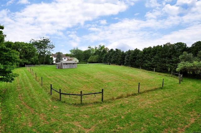 view of yard featuring a shed, fence, an outdoor structure, and a rural view