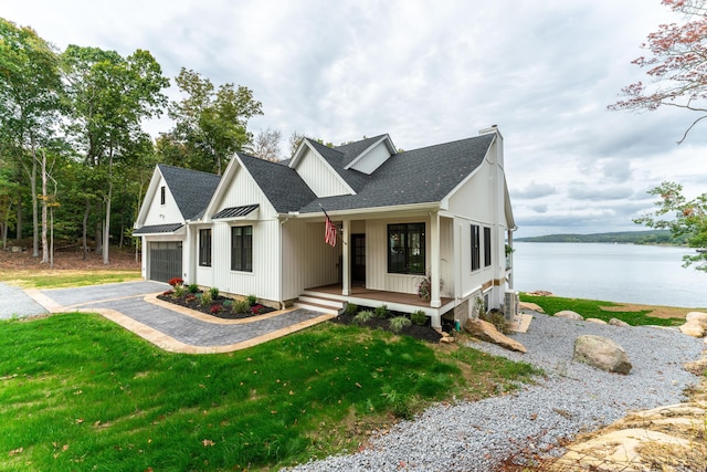 modern farmhouse with a front yard, a porch, a water view, and a garage