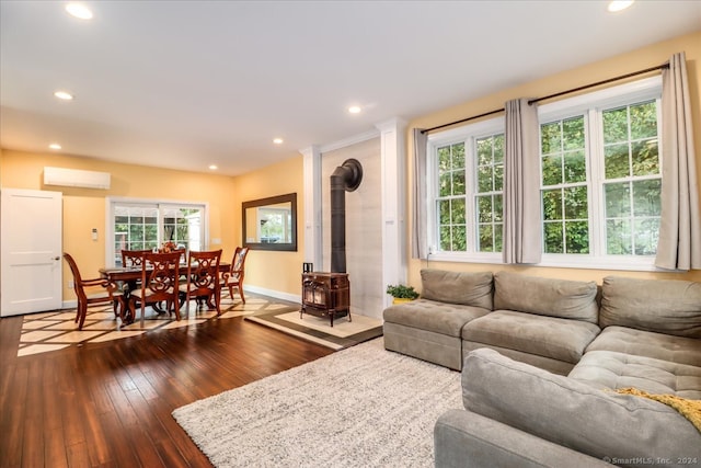 living room with a wall mounted air conditioner, a wealth of natural light, a wood stove, and hardwood / wood-style flooring