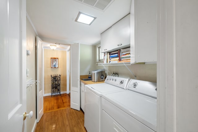 clothes washing area featuring washer and dryer, crown molding, cabinets, and light hardwood / wood-style flooring