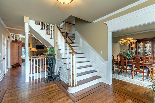 staircase with decorative columns, ornamental molding, an inviting chandelier, and hardwood / wood-style floors