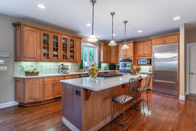 kitchen featuring built in appliances, backsplash, a center island, pendant lighting, and dark hardwood / wood-style flooring