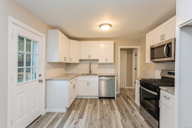 kitchen with appliances with stainless steel finishes, sink, light stone counters, light wood-type flooring, and white cabinets