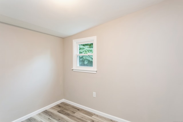 spare room featuring light wood-type flooring and vaulted ceiling