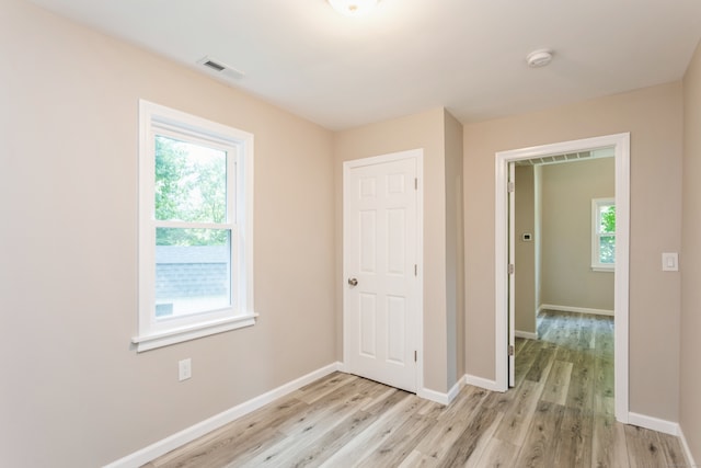 unfurnished bedroom featuring light hardwood / wood-style flooring, multiple windows, and a closet