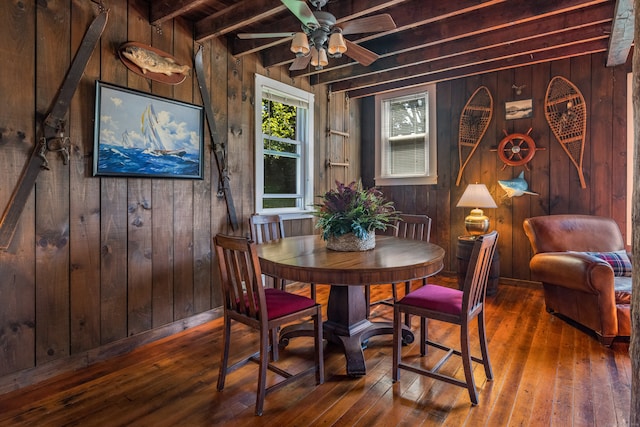 dining area with beamed ceiling, ceiling fan, wooden walls, and dark hardwood / wood-style floors