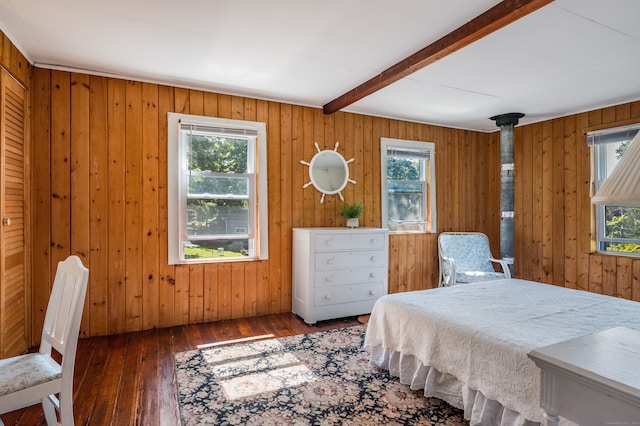 bedroom with beamed ceiling, wood walls, a wood stove, and dark hardwood / wood-style floors