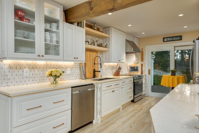 kitchen with wall chimney exhaust hood, sink, white cabinets, light stone counters, and stainless steel appliances