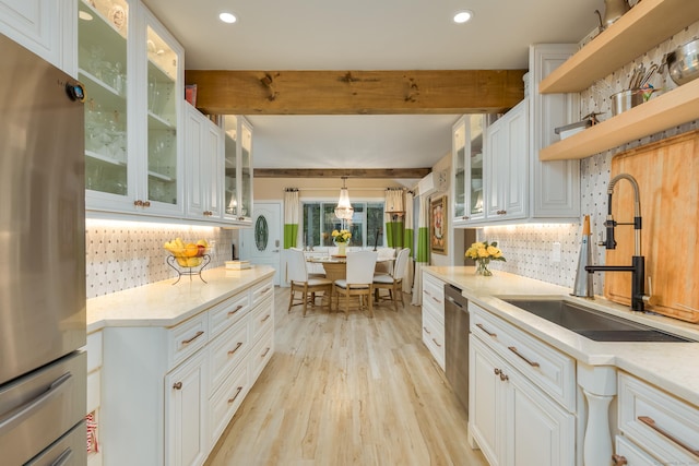 kitchen with hanging light fixtures, appliances with stainless steel finishes, sink, white cabinets, and beam ceiling