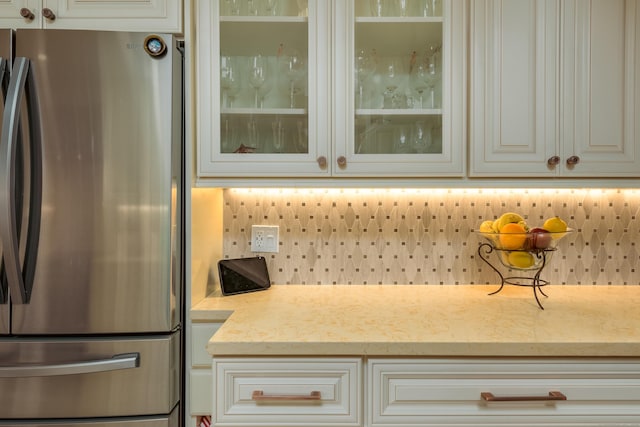 kitchen with decorative backsplash, light stone countertops, white cabinetry, and stainless steel refrigerator