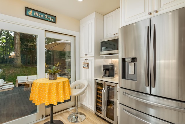 kitchen with light wood-type flooring, stainless steel appliances, white cabinetry, and beverage cooler