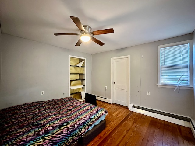 unfurnished bedroom featuring a walk in closet, ceiling fan, baseboard heating, and wood-type flooring