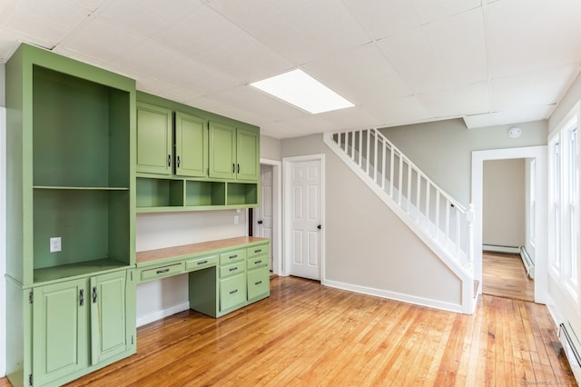 unfurnished office featuring built in desk, baseboard heating, and light wood-type flooring