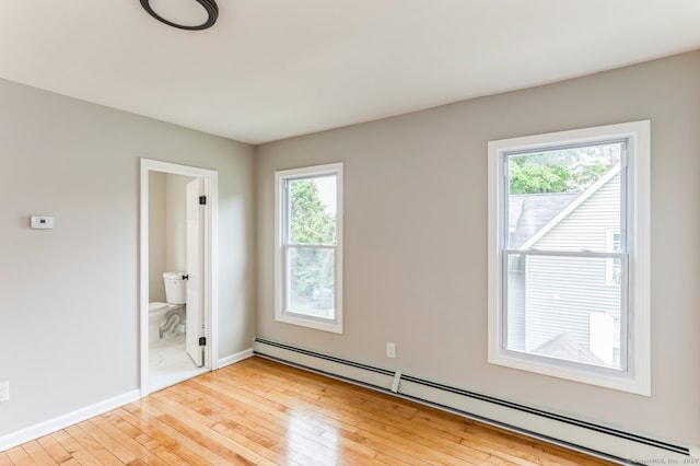 empty room with light hardwood / wood-style flooring, baseboard heating, and a healthy amount of sunlight