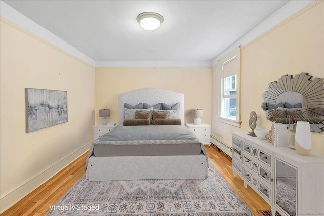 bedroom with ornamental molding, a baseboard heating unit, and light hardwood / wood-style flooring