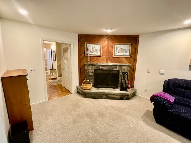 living room featuring carpet flooring, wooden walls, and a stone fireplace