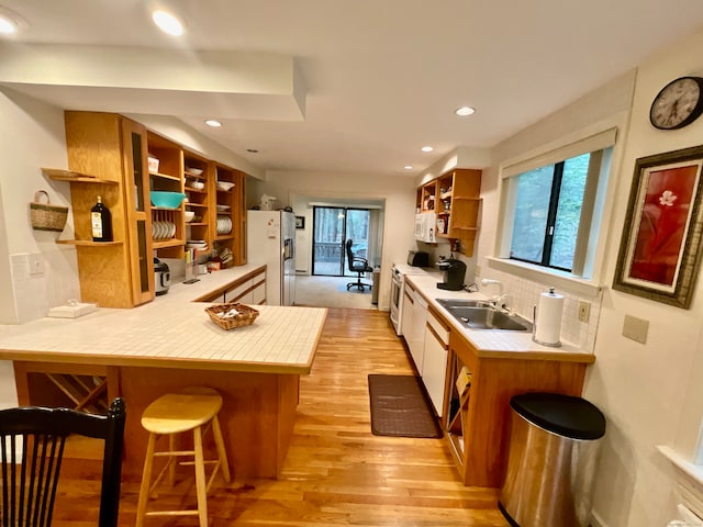 kitchen with kitchen peninsula, white appliances, a kitchen breakfast bar, tile counters, and light hardwood / wood-style floors