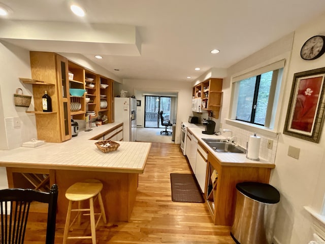 kitchen with a kitchen breakfast bar, open shelves, light countertops, light wood-type flooring, and white appliances