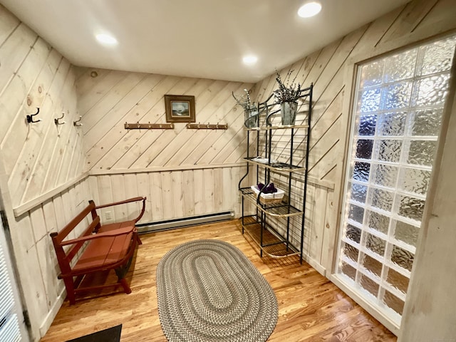 sitting room featuring a baseboard heating unit, wooden walls, and light wood-style floors