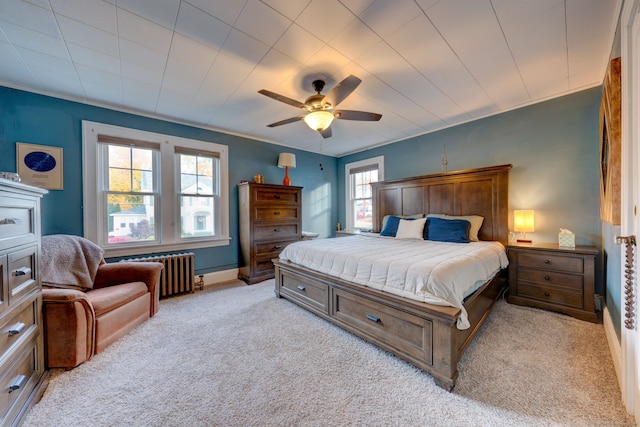 bedroom with crown molding, baseboards, radiator heating unit, light carpet, and a ceiling fan