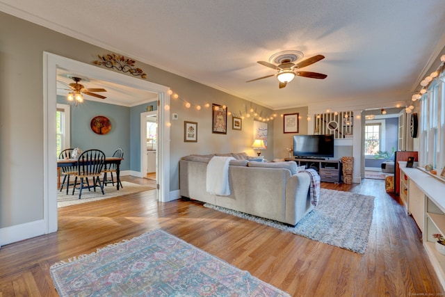 living room featuring ceiling fan, crown molding, baseboards, and wood finished floors