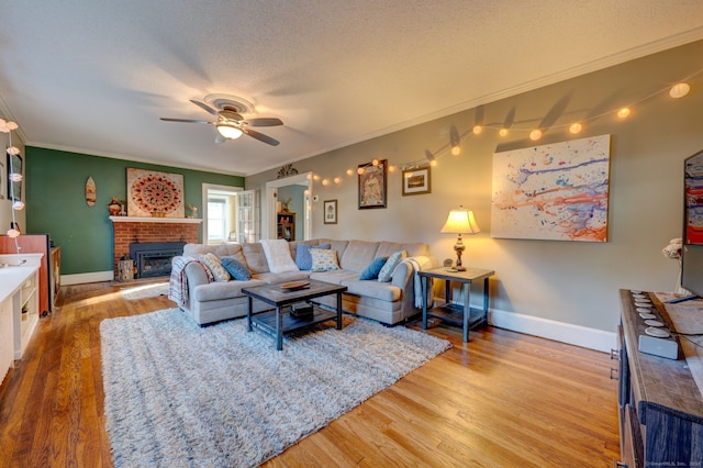 living area featuring light wood-style floors, ornamental molding, a fireplace, and a textured ceiling