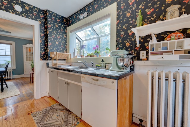 kitchen featuring wallpapered walls, light wood-style flooring, white dishwasher, a sink, and tile counters