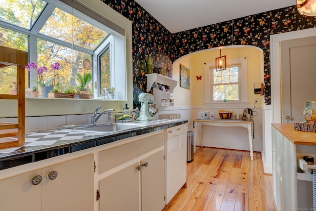 kitchen with light wood finished floors, wallpapered walls, tile counters, white dishwasher, and a sink