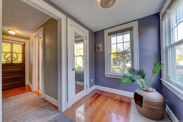 doorway to outside featuring baseboards, light wood finished floors, and a textured ceiling