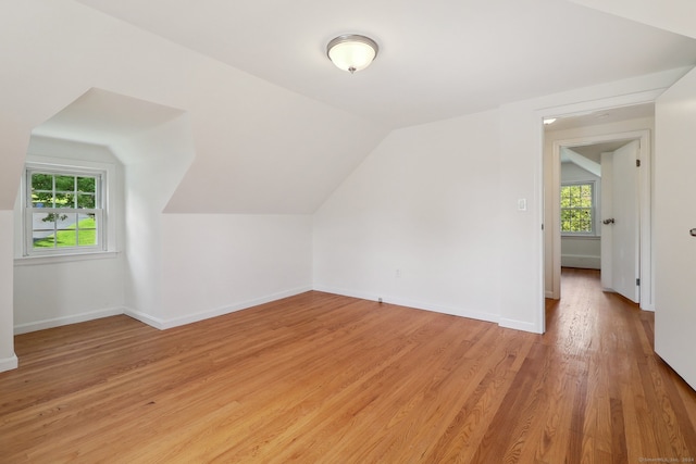 additional living space featuring light hardwood / wood-style floors, a healthy amount of sunlight, and lofted ceiling