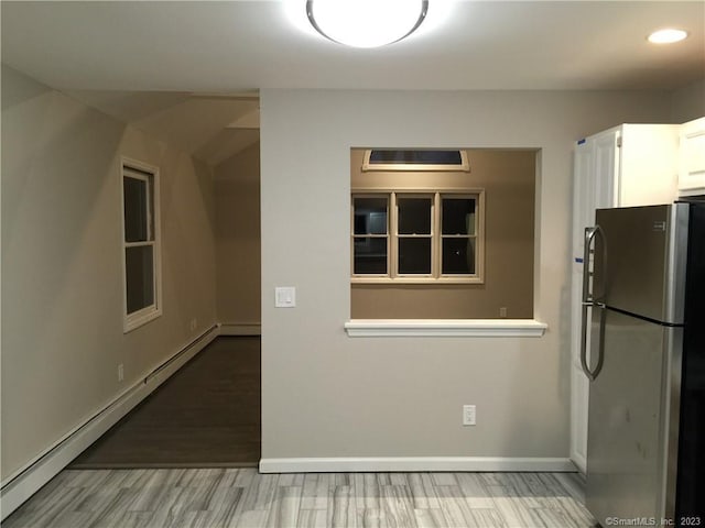 kitchen with stainless steel fridge, hardwood / wood-style floors, baseboard heating, and white cabinetry