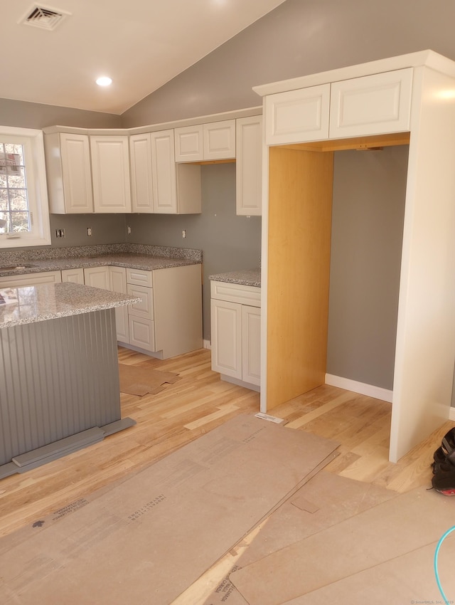 kitchen with light stone counters, white cabinets, light hardwood / wood-style flooring, and vaulted ceiling