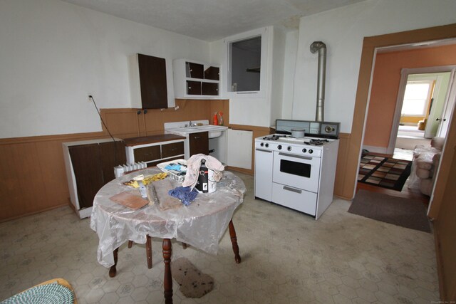 kitchen featuring white stove, wood walls, and white cabinetry