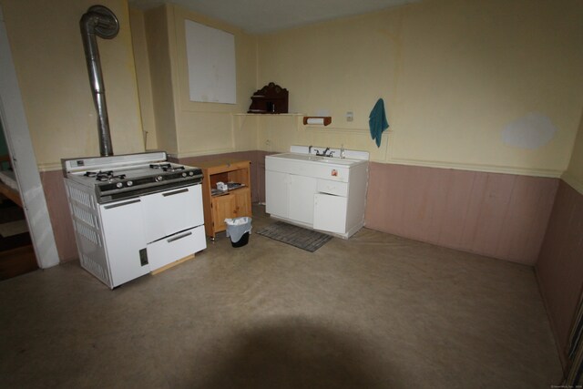 kitchen featuring light colored carpet, wood walls, sink, and white range with gas cooktop