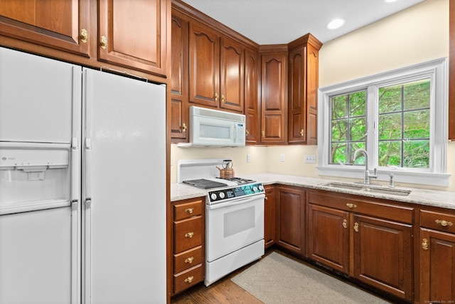 kitchen with light hardwood / wood-style flooring, white appliances, light stone counters, and sink