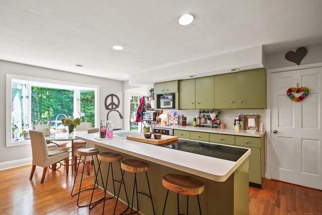 kitchen with green cabinetry, dark hardwood / wood-style flooring, a kitchen breakfast bar, decorative backsplash, and a center island with sink