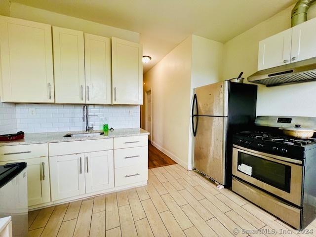 kitchen featuring white cabinets, appliances with stainless steel finishes, light stone counters, light hardwood / wood-style floors, and sink