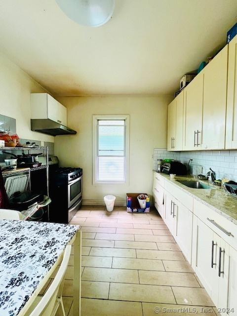 kitchen with a sink, backsplash, stainless steel range with gas cooktop, and under cabinet range hood