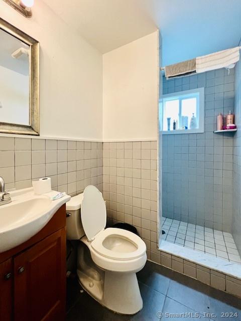 bathroom featuring tile patterned flooring, toilet, vanity, tile walls, and a shower stall