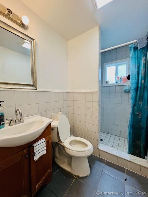 bathroom with tile patterned flooring, toilet, vanity, tile walls, and tiled shower