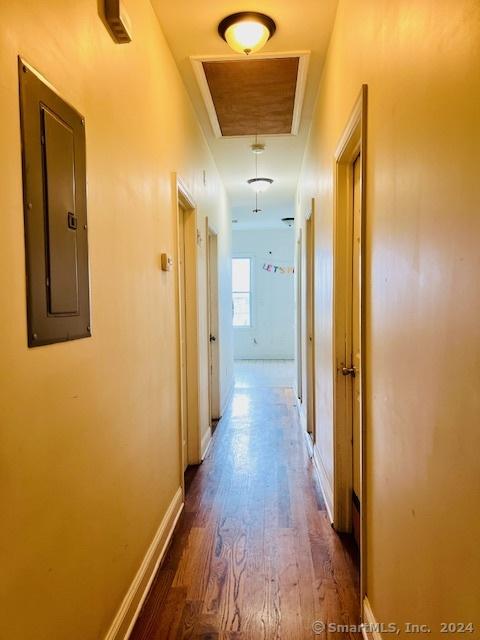 hallway featuring attic access, electric panel, baseboards, and wood finished floors