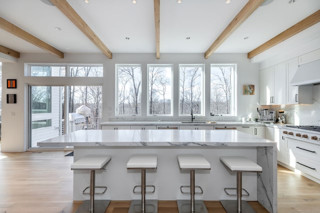 kitchen featuring a breakfast bar area, light stone countertops, and beam ceiling