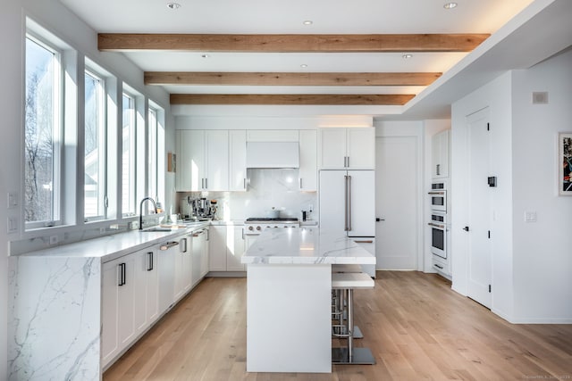 kitchen with a kitchen island, a healthy amount of sunlight, beamed ceiling, and light hardwood / wood-style floors