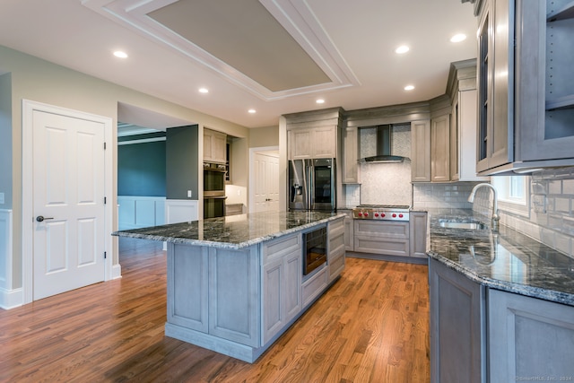 kitchen featuring black appliances, hardwood / wood-style floors, sink, wall chimney range hood, and dark stone counters