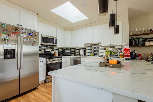 kitchen with a skylight, hanging light fixtures, light stone countertops, stainless steel appliances, and white cabinetry