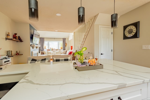 kitchen featuring hanging light fixtures, light stone countertops, and white cabinetry