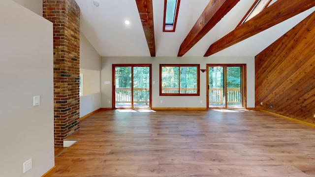 unfurnished living room with vaulted ceiling with skylight, wooden walls, and light hardwood / wood-style floors