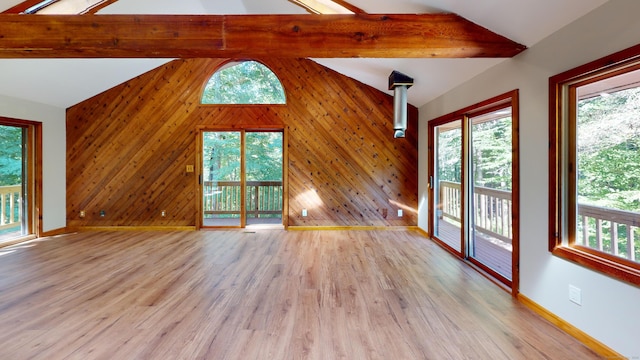 unfurnished living room with light hardwood / wood-style flooring, lofted ceiling with beams, and a healthy amount of sunlight