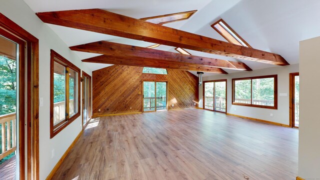 unfurnished living room with wooden walls, lofted ceiling with skylight, and a healthy amount of sunlight