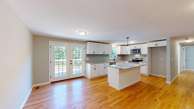 kitchen featuring white cabinets, hanging light fixtures, light hardwood / wood-style flooring, appliances with stainless steel finishes, and a kitchen island